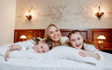 Gülünecek bir anne ve ikiz çocukları rahat bir oda bir yatakta yatarken portresi.