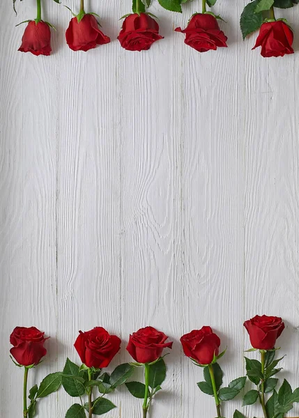 Frame of red roses on white wooden background. With space for text