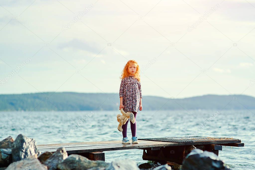 A lonely girl with a plush Bunny is standing on the pier and looks into the distance at the sea