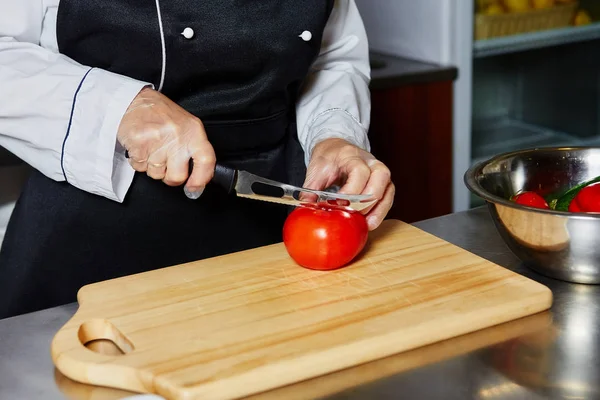 Chef cutting tomato on cutting board.