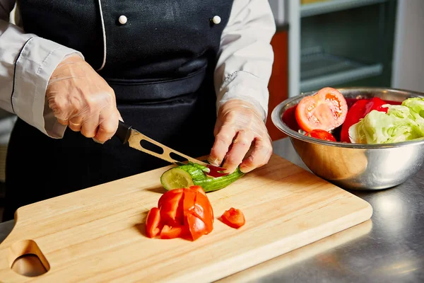 Chef cutting tomato on cutting board.