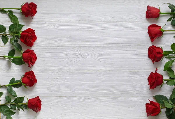 Frame of red roses on white wooden background. With space for text