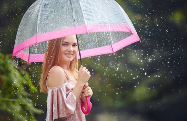 Bir genç kız parkta yürürken yağmur bir şemsiye altında saklandım. O gülüyor ve gülümsüyor, sıcak ve yağışlı havalarda sevinir