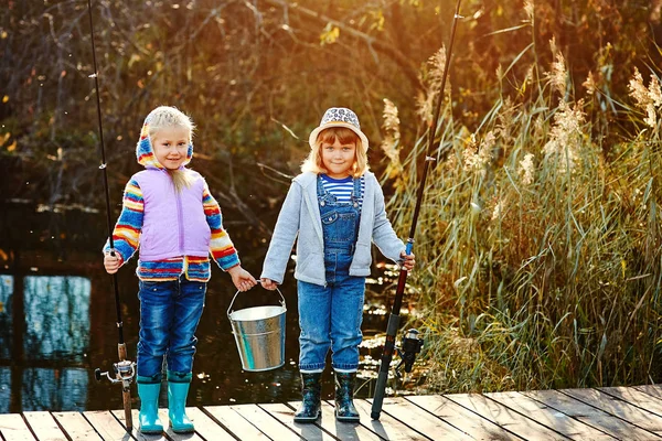 Дві дівчини стоять на мосту і тримають в руках рибальські палички і відро для риби — стокове фото