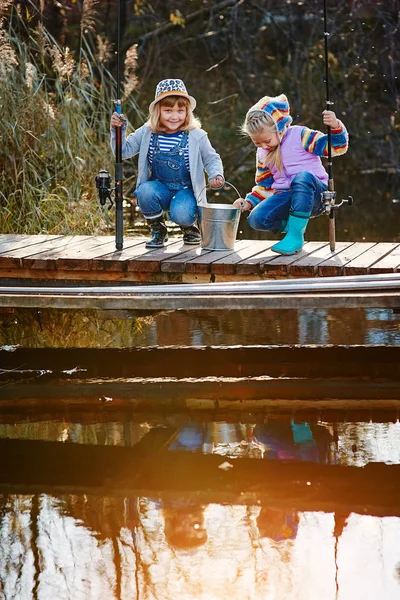 Дві маленькі дівчата з рибальськими паличками, сидять на дерев'яному понтоні і хвалиться спійманою рибою — стокове фото