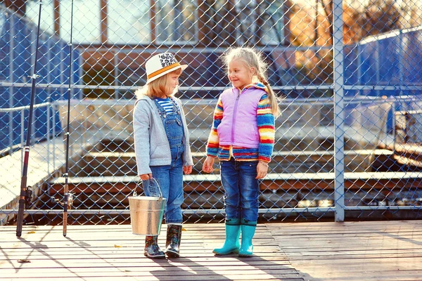 Two happy laughing children with fishing rods and a bucket on a fishing trip on a wooden pontoon on a fish farm — Stock Photo, Image