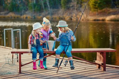 Üç küçük mutlu kız bir olta kamışı yakalanan balık hakkında övünme. Ahşap bir duba Balık tutma. 