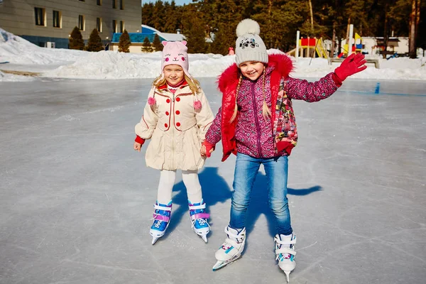 Two little smiling girls ride on the ice in bright casual clothes. Skate rental in the hotel. Outdoors.