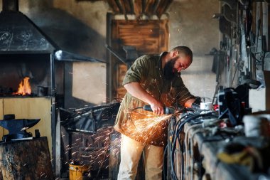 Sakallı bir işçi bir bölümü bir açı öğütücü ile keser. Kıvılcımlar.