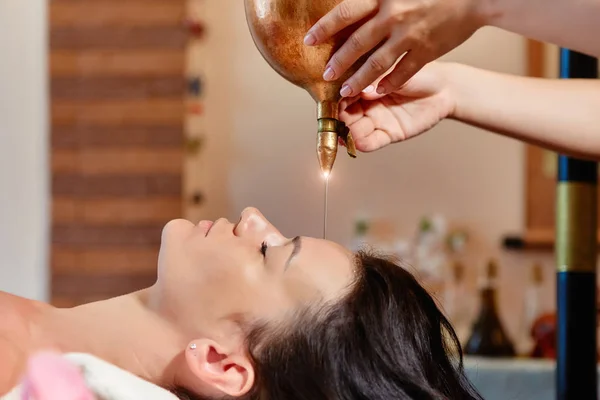 Shirodhara, een Ayurvedische genezings techniek. Olie druipend op het vrouwelijke voorhoofd. Portret van een jonge vrouw tijdens een Ayurvedische massagesessie met aromatische olie druipend op haar voorhoofd en haar — Stockfoto