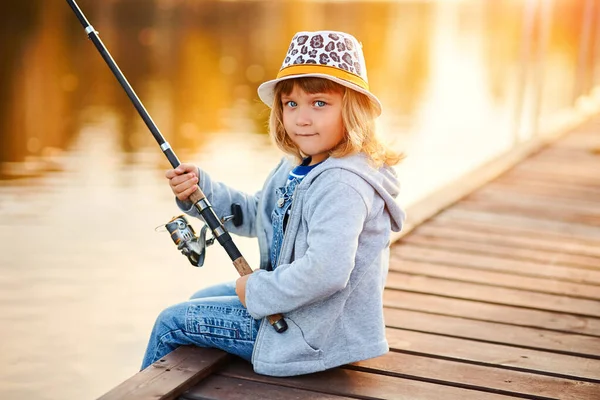Una niña pescando desde el muelle en el estanque en la mañana soleada — Foto de Stock