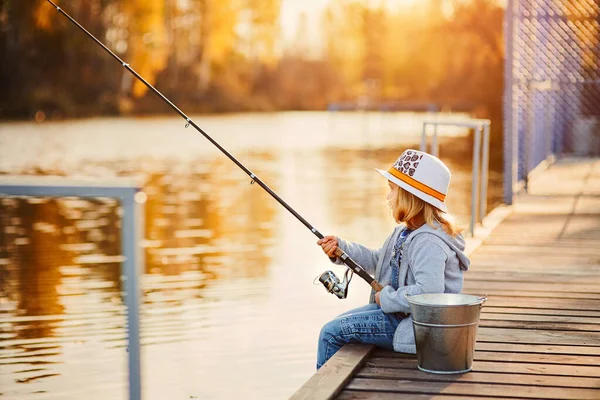 Una niña pescando desde el muelle en el estanque en la mañana soleada — Foto de Stock