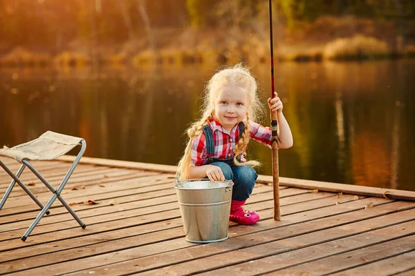 Niña pescadora con una caña de pescar y un cubo de pescado en un muelle de madera . —  Fotos de Stock