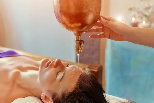 Ayurveda Massage alternative Heiltherapie. Schöne kaukasische Frau bekommt Shirodhara Behandlung liegend auf einem Holztisch im indischen Salon. — Stockfoto