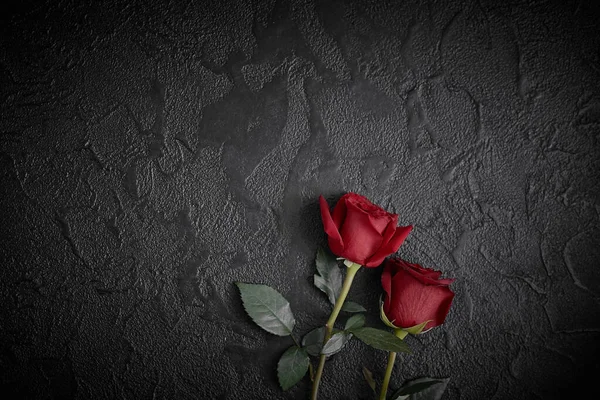 Les roses rouges sont placées sur un fond texturé noir. Un signe de condoléances, une perte de sympathie. Espace pour votre texte . — Photo