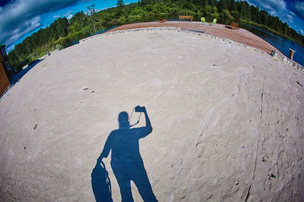 A self-portrait of a photographer with a camera in his hands casts a shadow on the sandy ground with a silhouette — Stock Photo, Image