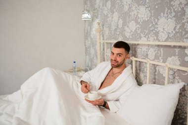 Seksi genç adam yatakta yatarken kameraya bakıyor..