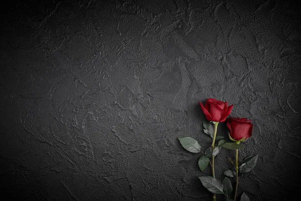 Rose rosse sono collocati su uno sfondo nero strutturato. Un segno di condoglianze, perdita di compassione. Spazio per il testo — Foto Stock