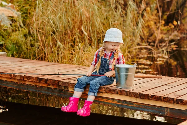 Una niña con una caña de pescar mira la captura de peces en un cubo —  Fotos de Stock