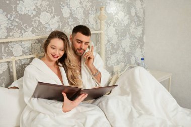 Yatakta yatan genç çift otel restoranından yemek sipariş etmek için oda servisini arıyor.