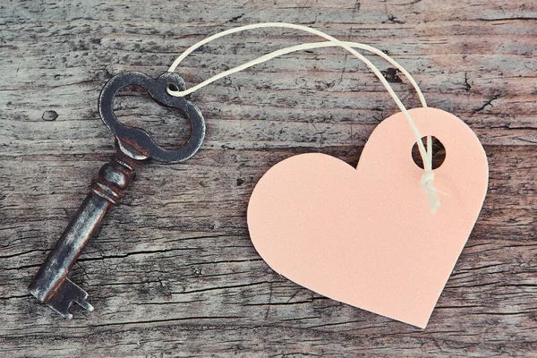 Una llave hecha a mano antigua con un llavero de etiqueta en forma de corazón se encuentra en un tablero de madera — Foto de Stock
