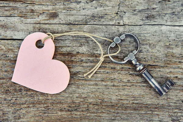 Una llave hecha a mano antigua con un llavero de etiqueta en forma de corazón se encuentra en un tablero de madera — Foto de Stock
