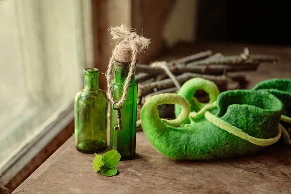 Chaussures vertes feutrées colorées se tiennent à côté de bouteilles en verre antique, une feuille de trèfle et un paquet de bois de chauffage — Photo