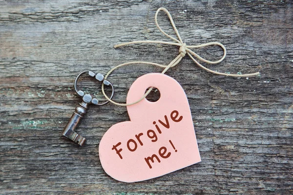 An apology card with the words forgive Me. A heart with an antique key lies together on a wooden Board. The concept of reconciliation. The view from the top