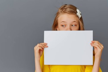 Gri arka planda sarı elbiseli genç bir kız konsept için beyaz bir poster tutuyor..