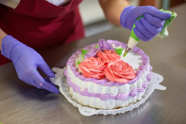 Pastry chef decorates the cake with flowers from the cream. The cream is squeezed out of the pastry bag through a special nozzle.