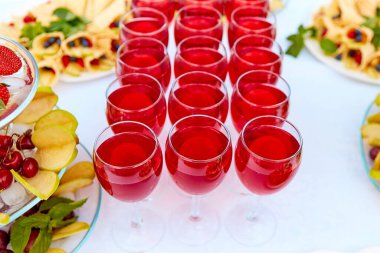 Bir sırada kırmızı içecekler, meyve suyu, şampanya ya da bir partide şarap. Yemek servisi. Masanın üzerinde beyaz bir masa örtüsü olan cam eşyalar. Bayram için açık büfe