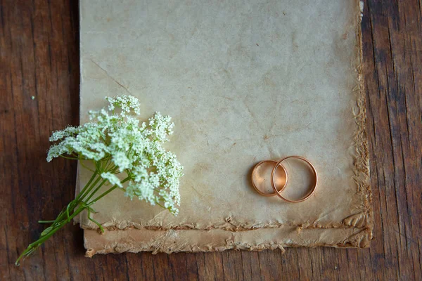 Wedding rings and a wild flower are on antique paper. Symbols of eternal love. Recognition on Valentine's day with a place for your text.