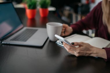 Çay içme ve modern smartphone sabah haber okuma Internet'e bağlıyken açık netbook bilgisayar ile masada oturan bir genç bayan. Modern teknoloji kullanan kadın kişi.