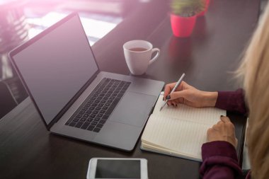 Kadın eli kalem kayıtları ile tarih seçici odak dizüstü bilgisayar ve smartphone ile masada oturan kağıt Not defteri programında planlanan. Yapmam gerekenler organizasyonu. Yaratıcı fikirler yazma.