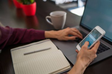 Seçici odak üstünde smartphone aygıt hangi kadın kişi rahat iç masada oturan açık açık dizüstü bilgisayar tutun. Cep telefonu ve dizüstü eşitleme kadın görünümünü kırpılmış.