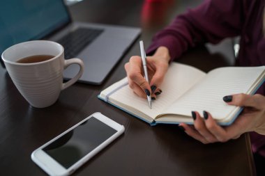 Elinde bardak çay ile masada oturan kağıt Defteri'nde notlar yazma kalemi ile kadın kişinin görünümü kadar yakın. Seçici odak üstünde defter, kız öğrencinin sınav kayıt bilgi için hazırlanıyor
