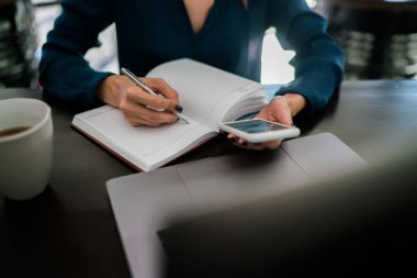 Kadın el seçici odaklı smartphone cep telefonu ile online bilgi okurken kağıt Not Defteri'nde notlar yazma kalemi ile yakın çekim. Tüm planlanan görevleri başarılı bir organizasyon garantisi olarak kaydetmek