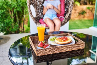 Bahçede bir sallanan sandalye üzerinde oturan kız. Ön planda bir parlak yaz kahvaltı.