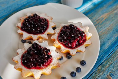 Bir büyük beyaz tabak aşçı ile dzheomo Svezhnev, yaban mersini, kuş üzümü ve yaban mersini taze pişmiş tartlets sundu