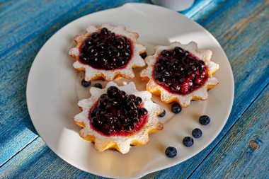 Bir büyük beyaz tabak aşçı ile dzheomo Svezhnev, yaban mersini, kuş üzümü ve yaban mersini taze pişmiş tartlets sundu