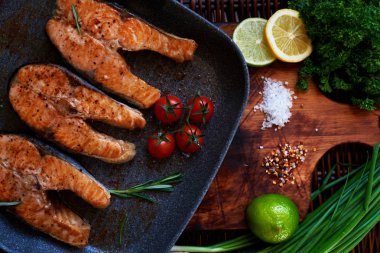 Konuklar için somon yemek biftek pişirmek için karım bekler, Balık biftek ızgara Pan rosemary ile ve domates, bir tava ile ahşap bir gemide kızarmış balık koymak