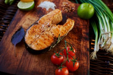 Büyük somon steak için hizmet balık mükemmel domates chives ve limon, ahşap bir yüzey üzerinde altın kahverengi yalan kadar fırında pişmiş somon ızgara parça pişmiş yemek Restoran