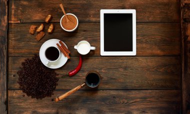 Karanlık dokusal ahşap bir masa üzerinde bir tablet yatıyor, bir fincan sütlü kahve Cezve artıkları güçlü siyah kahve