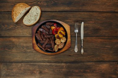 Koyu ahşap bir masa üzerinde dilim sulu et ve ızgara sebzeler ile dökme demir tavada, taze ekmek yakındadır