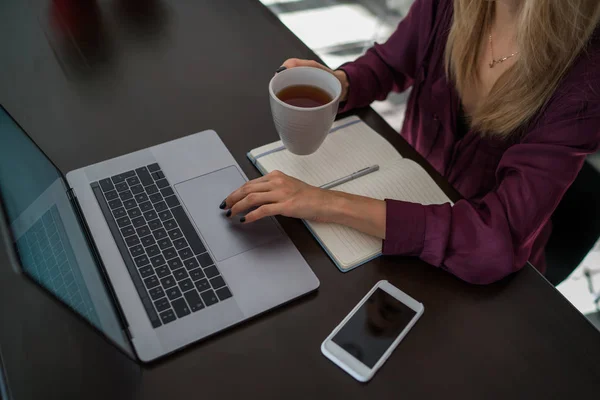 女人手捧着一杯饮料和键盘互联网要求的文字在上网本电脑上 有选择地专注于女性自由职业者在工作时饮用的茶杯 — 图库照片
