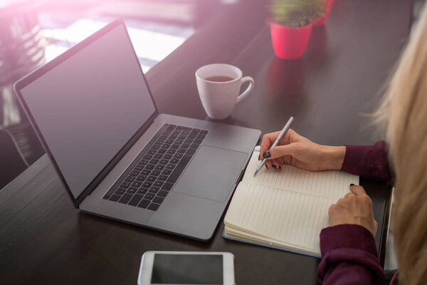 Селективное внимание на руку женщины с ручкой записи запланированное расписание в бумажном блокноте сидит за столом с ноутбуком и смартфоном. Организация вещей, которые нужно сделать. Написание творческих идей
.
