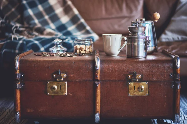 Old antique suitcase with coffee set against the backdrop of leather sofa with a cozy blanket. The concept of a comfortable pastime.