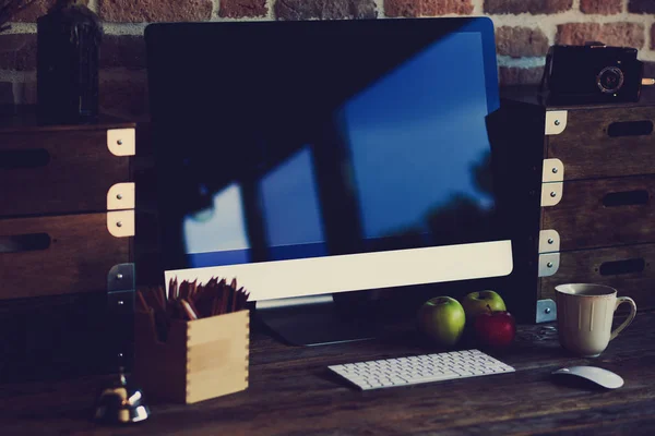 Comfortable workplace with big computer screen, mouse and keyboard. Wooden table with pencils for drawing and colorful apples.  Desktop with  cup of coffee and fresh apples for healthy breakfast.