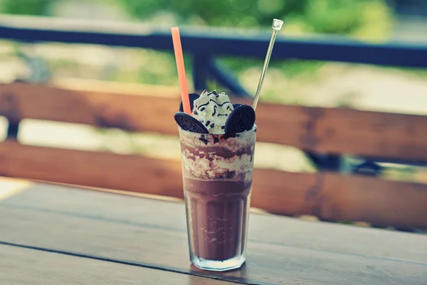Iced coffee with whipped cream and caramel ice cream in tall glass on rustic wooden table, selective focus. Cookies and  coffee in the coffee shop with blur outdoor background, selective focus