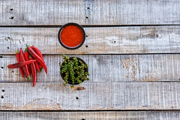Chili, chili sauce, green peppercorns on an old wooden table. Asian food concept. Top view. Copy space.